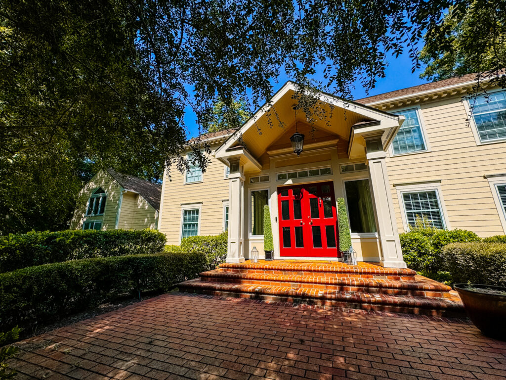 the exterior of a house. The house has pale yellow walls and a bright red front door.